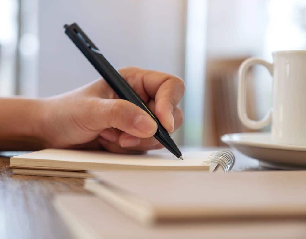 Menschliche Hand beim Scheiben mit schwarzen Stift auf Notizblock 